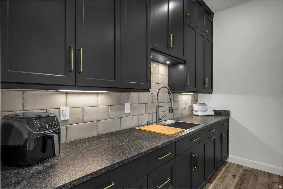 Kitchen featuring dark cabinetry, light wood-style flooring, decorative backsplash, and dark stone counters