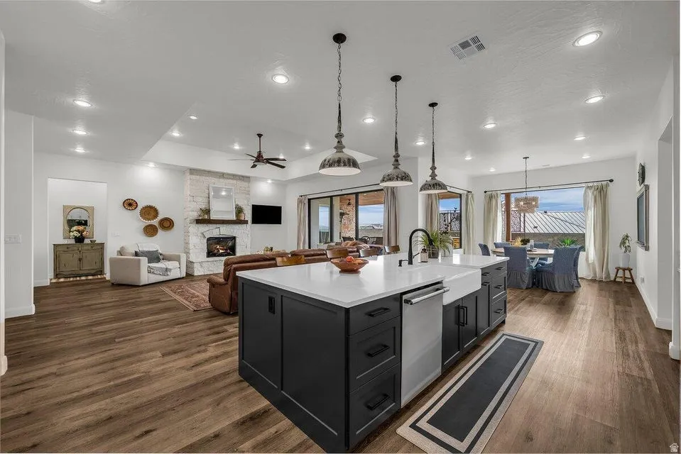 Kitchen featuring dark cabinetry, a kitchen island with sink, open floor plan, a fireplace, and dark wood-style flooring