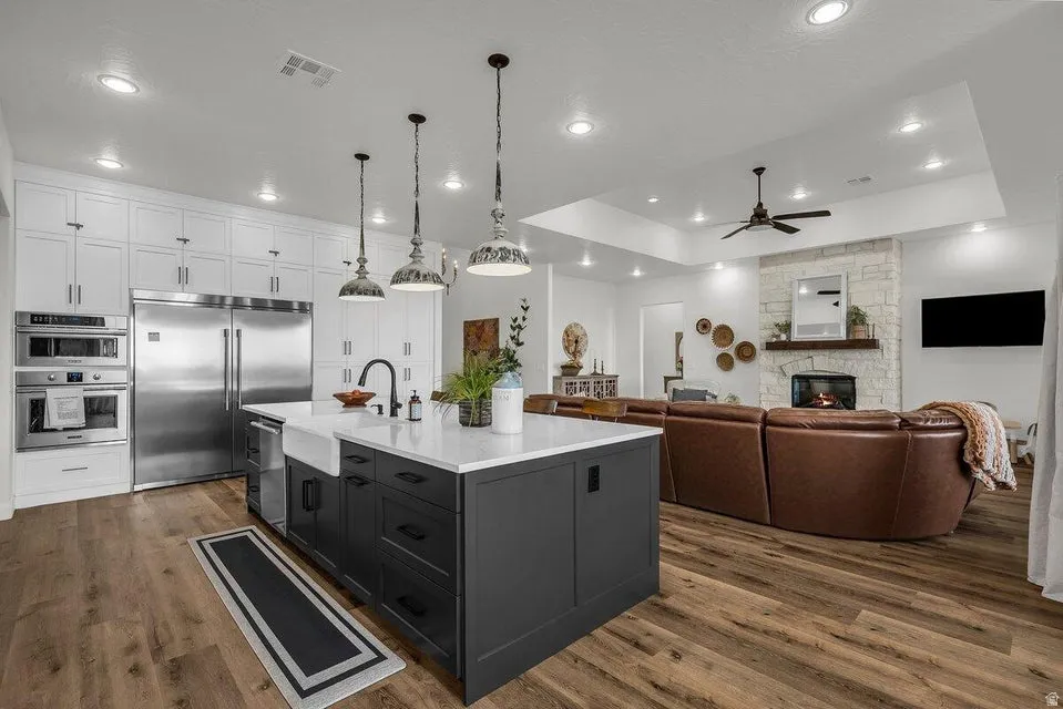 Dual tone kitchen with two tone cabinetry, stainless steel appliances, dark wood-type flooring, a kitchen island with sink, and a ceiling fan