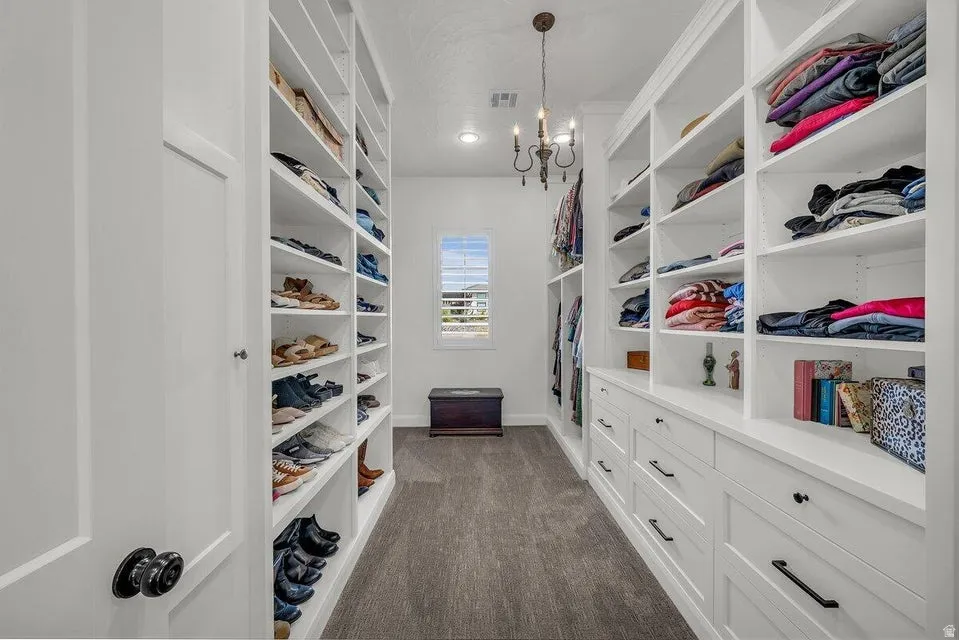 Walk in closet with suspended lighting and dark colored carpet