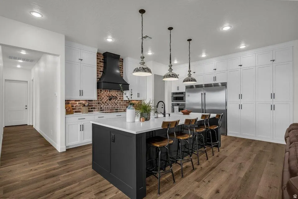 Kitchen with a kitchen bar, stainless steel appliances, a large island with sink, dark wood-style flooring, and two tone cabinets