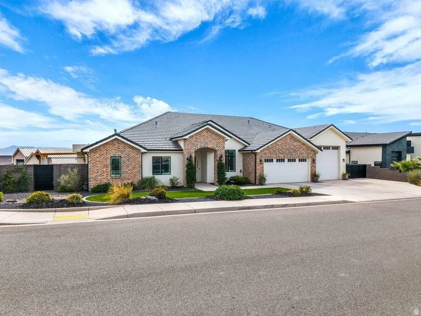 Single story home with a garage, driveway, brick siding, stucco siding, and a tiled roof