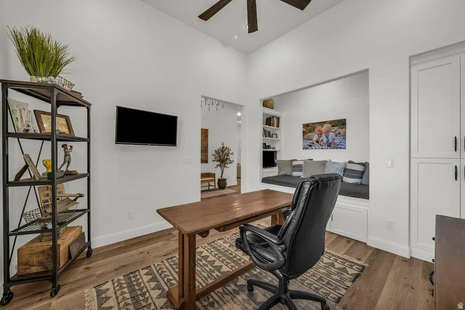 Office area with built in shelves, dark wood finished floors, ceiling fan, and a high ceiling