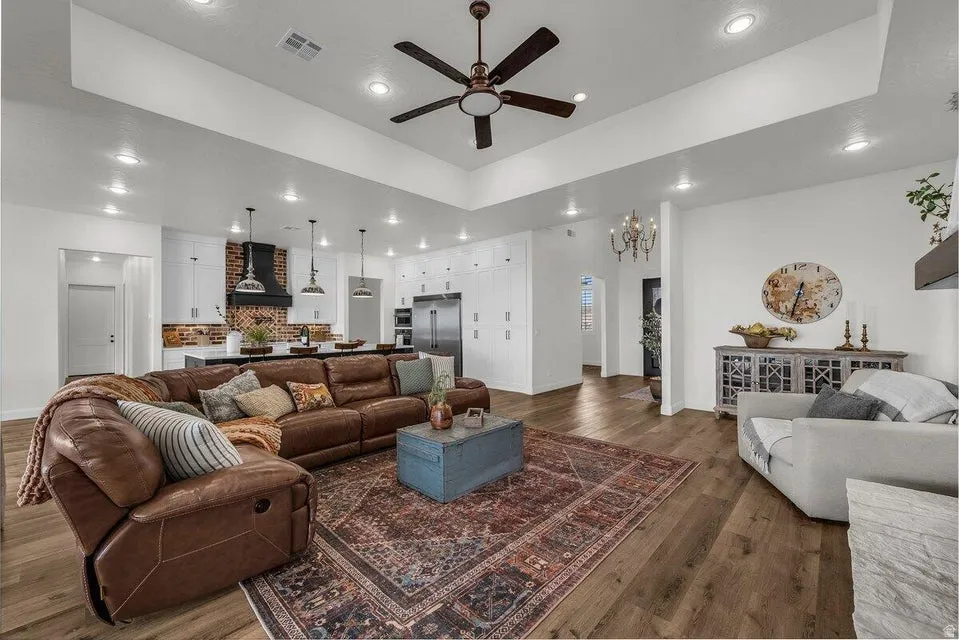 Living area with ceiling fan, dark wood-type flooring, a raised ceiling, and suspended lighting