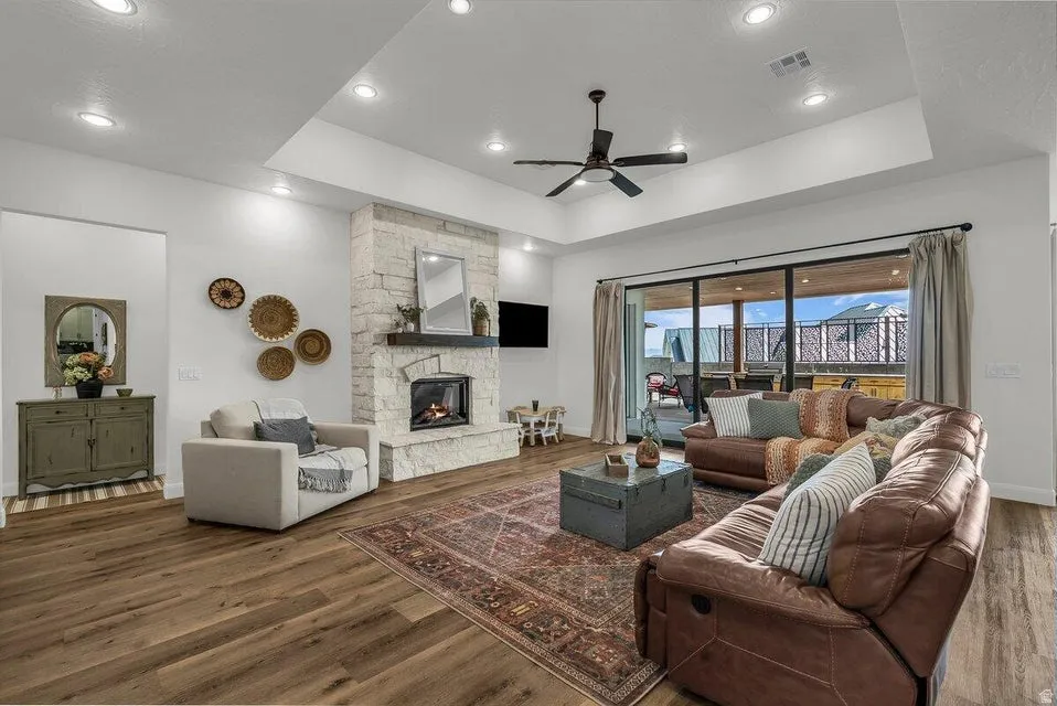 Living area featuring wood finished floors, ceiling fan, a fireplace, a tray ceiling, and recessed lighting