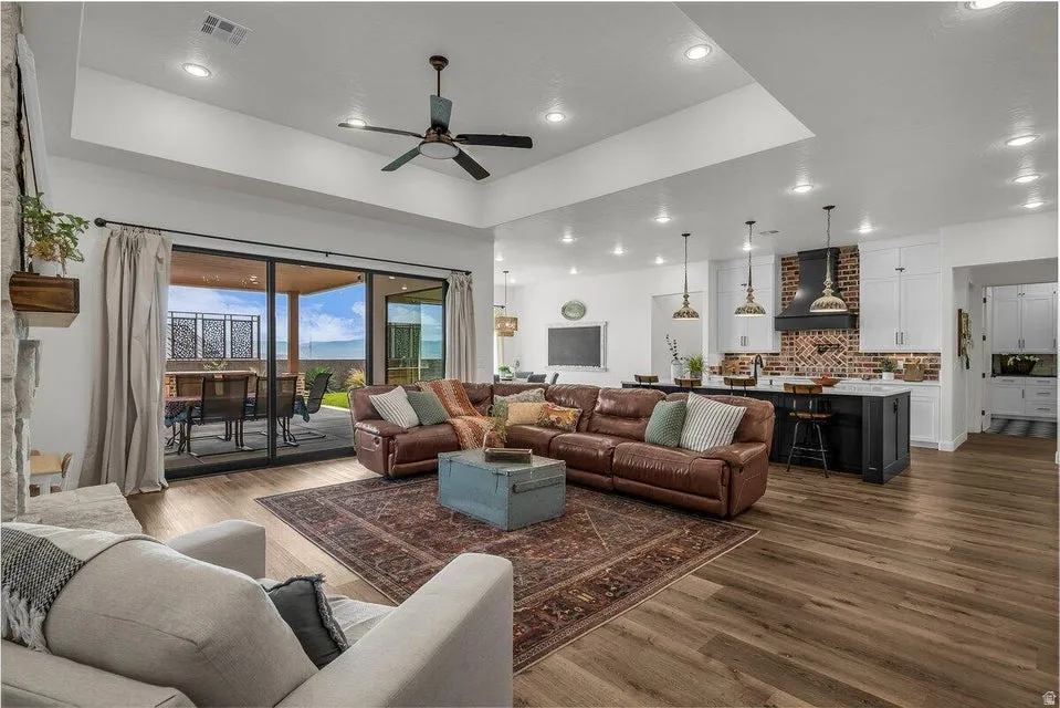 Living room with dark wood-style flooring, ceiling fan, a raised ceiling, and recessed lighting