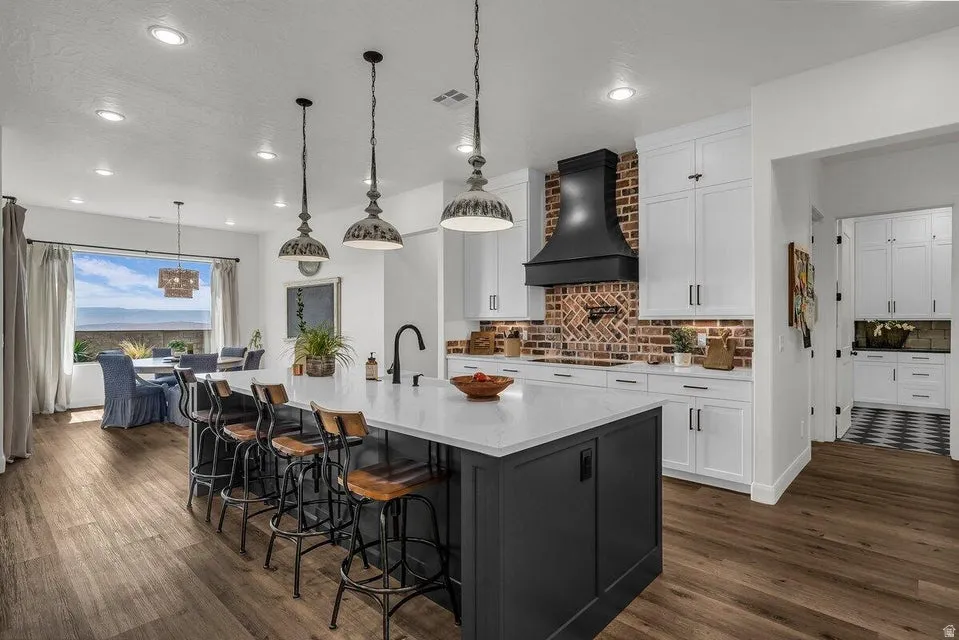 Kitchen featuring two tone cabinets, a breakfast bar, decorative backsplash, a large island with sink, and light stone counters