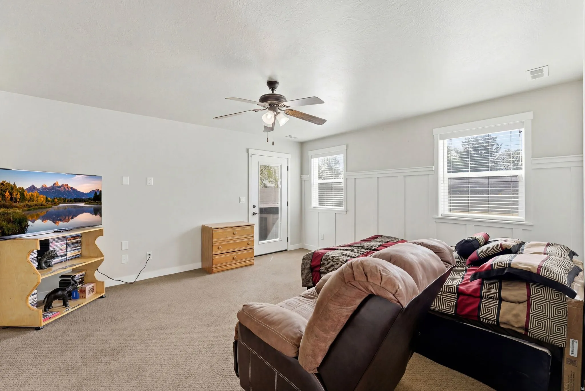 Carpeted living area featuring a decorative wall, wainscoting, and ceiling fan
