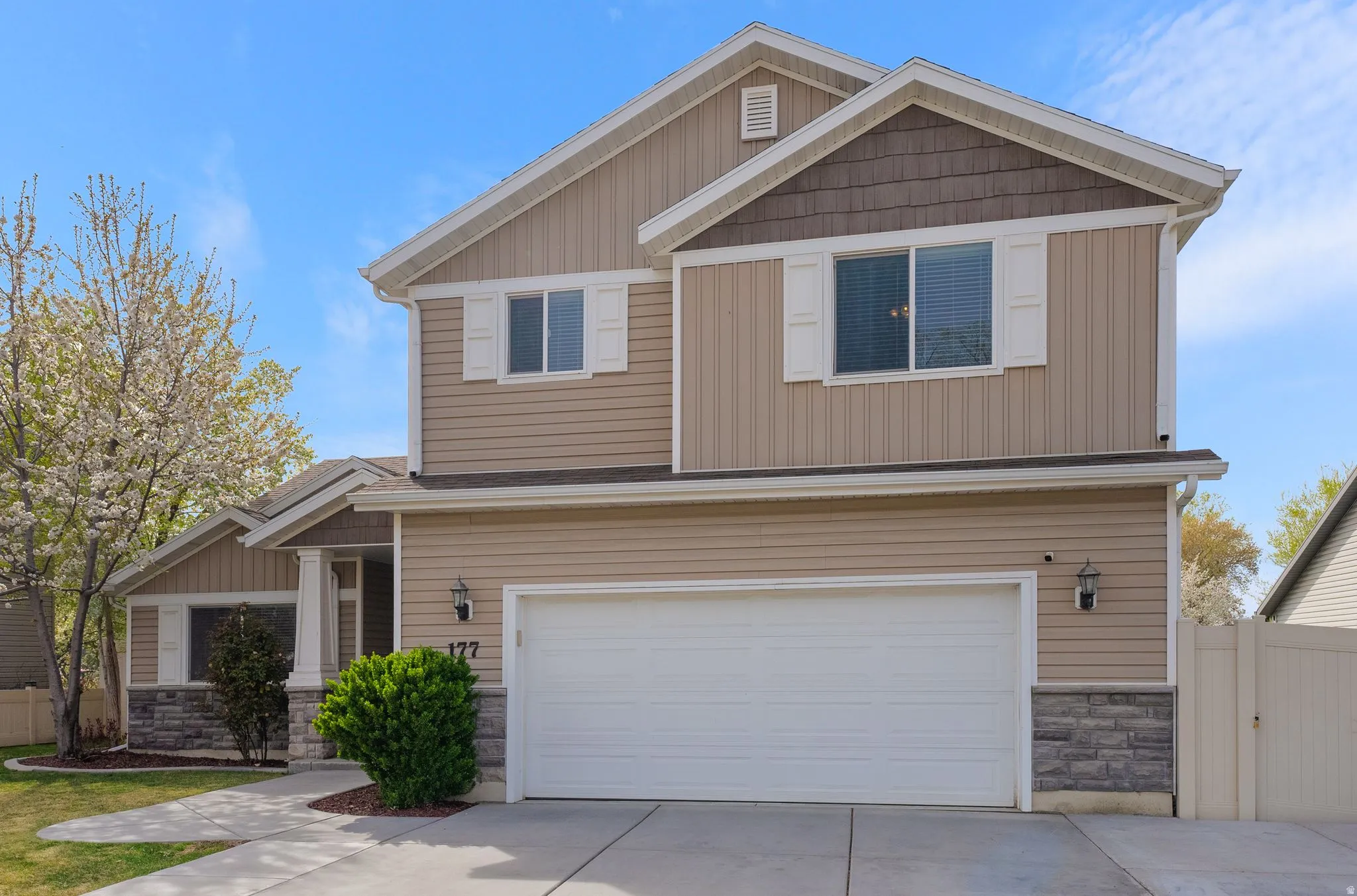 Craftsman house featuring stone siding, a garage, driveway, and a gate