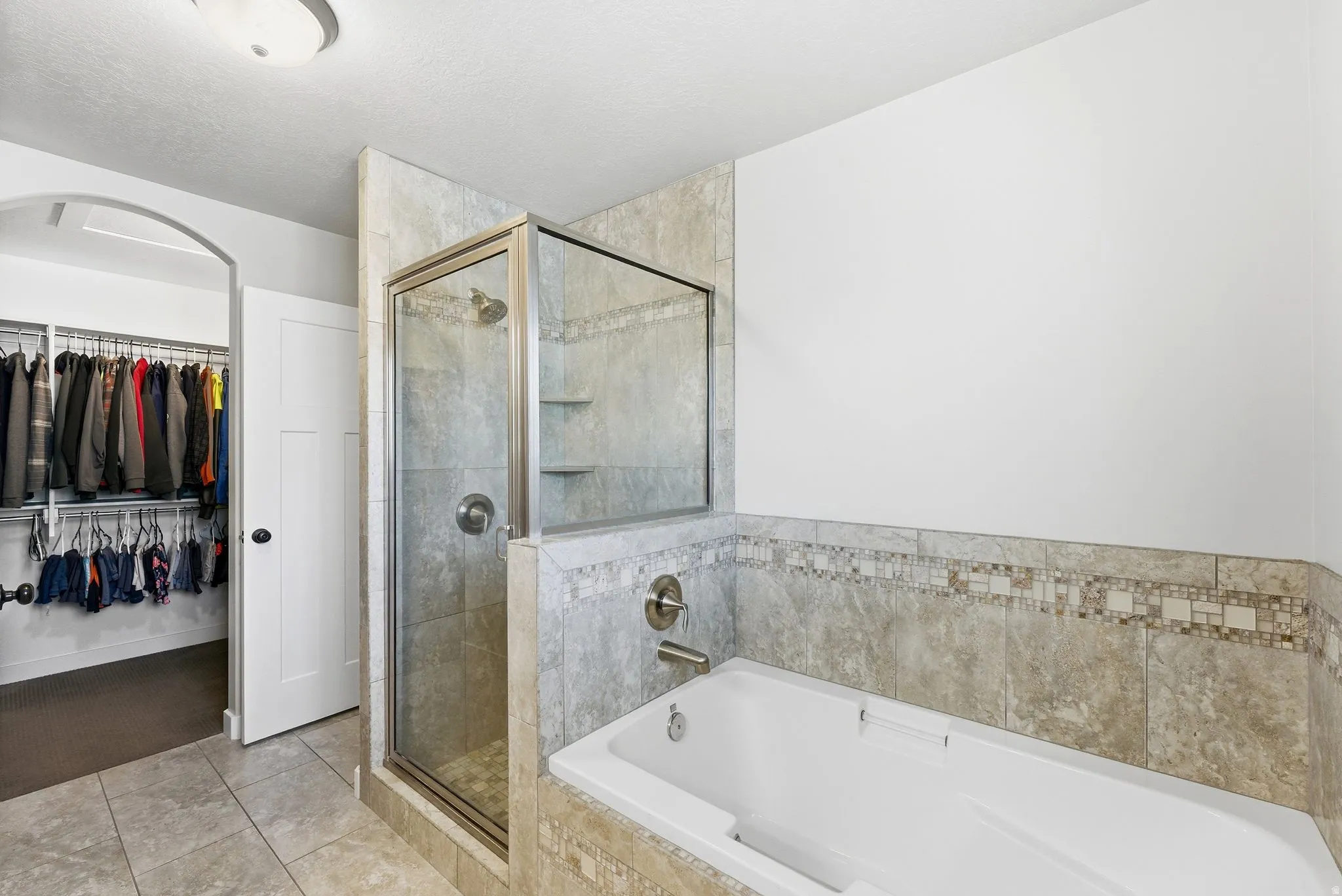 Full bath with a walk in closet, light tile patterned floors, a shower stall, and a bath