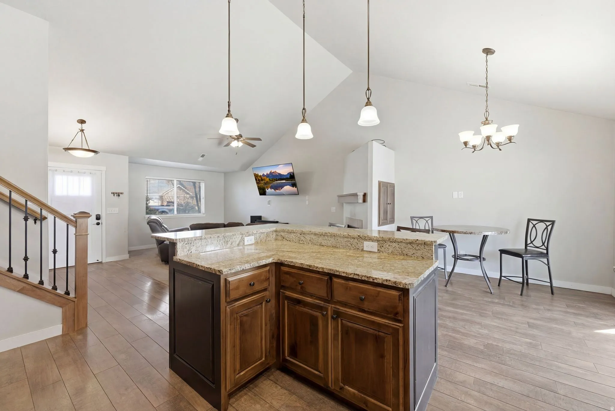 Kitchen with light stone counters, light wood-type flooring, a kitchen island, a ceiling fan, and a high ceiling