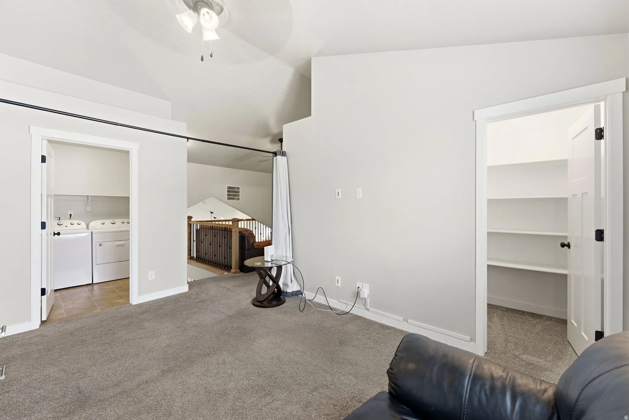 Unfurnished bedroom with light colored carpet, a spacious closet, washer and dryer, and vaulted ceiling