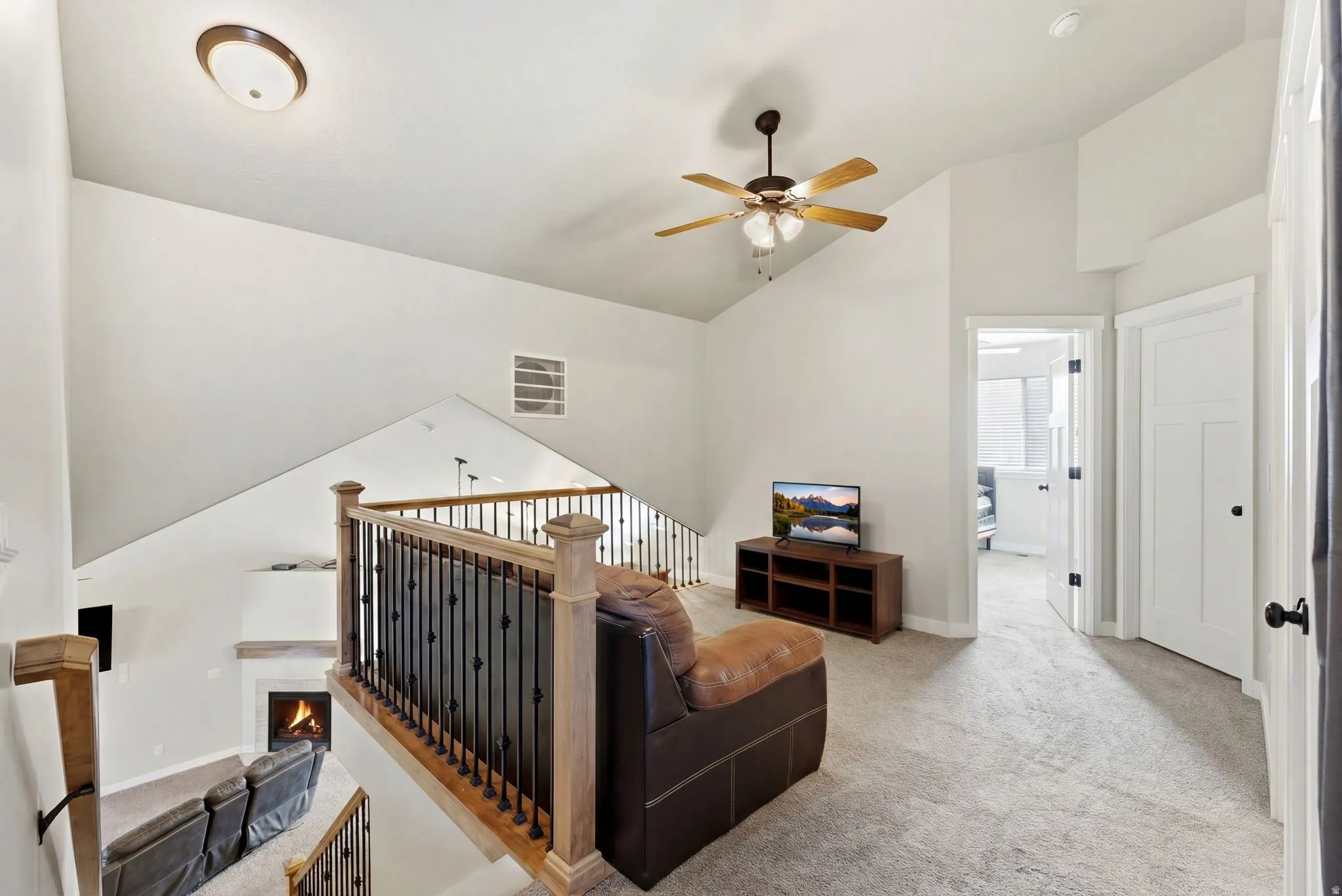 Carpeted living room with a ceiling fan, a lit fireplace, and lofted ceiling