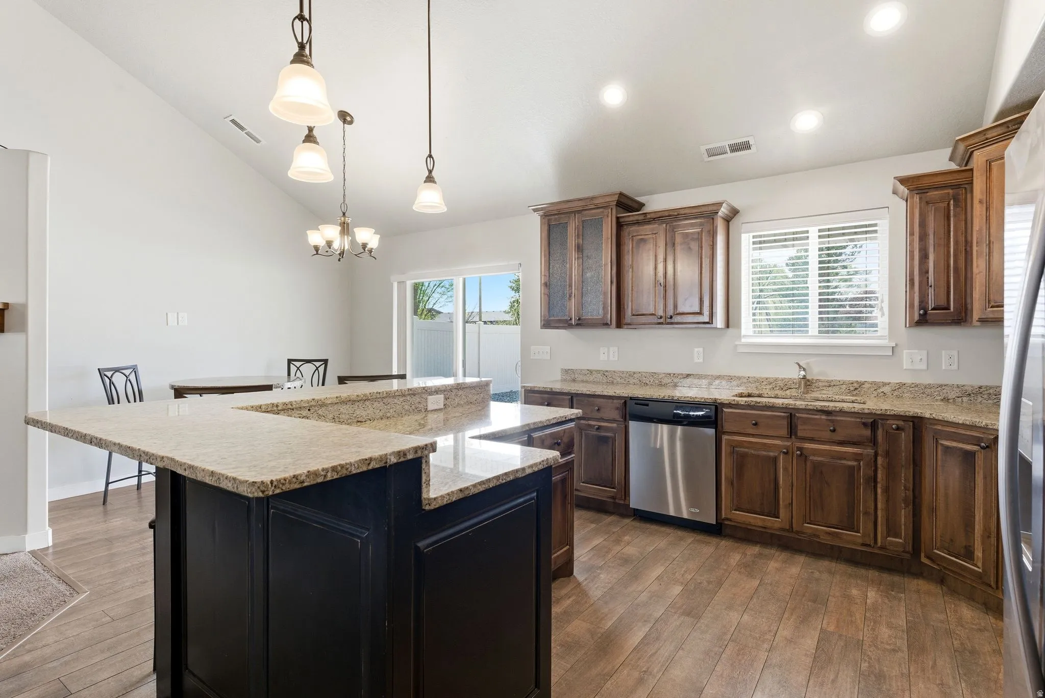 Kitchen with lofted ceiling, stainless steel appliances, light stone counters, dark wood finished floors, and a center island
