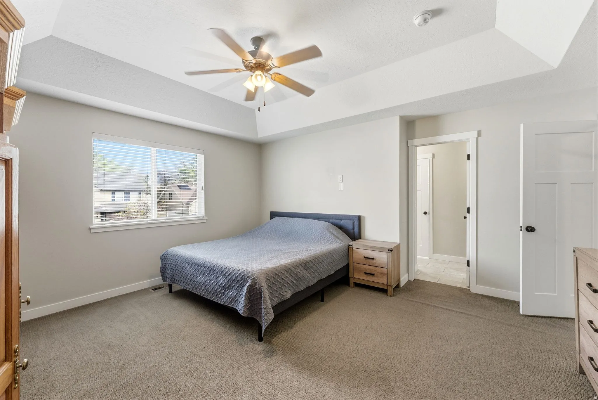 Bedroom with light colored carpet, a ceiling fan, and a raised ceiling