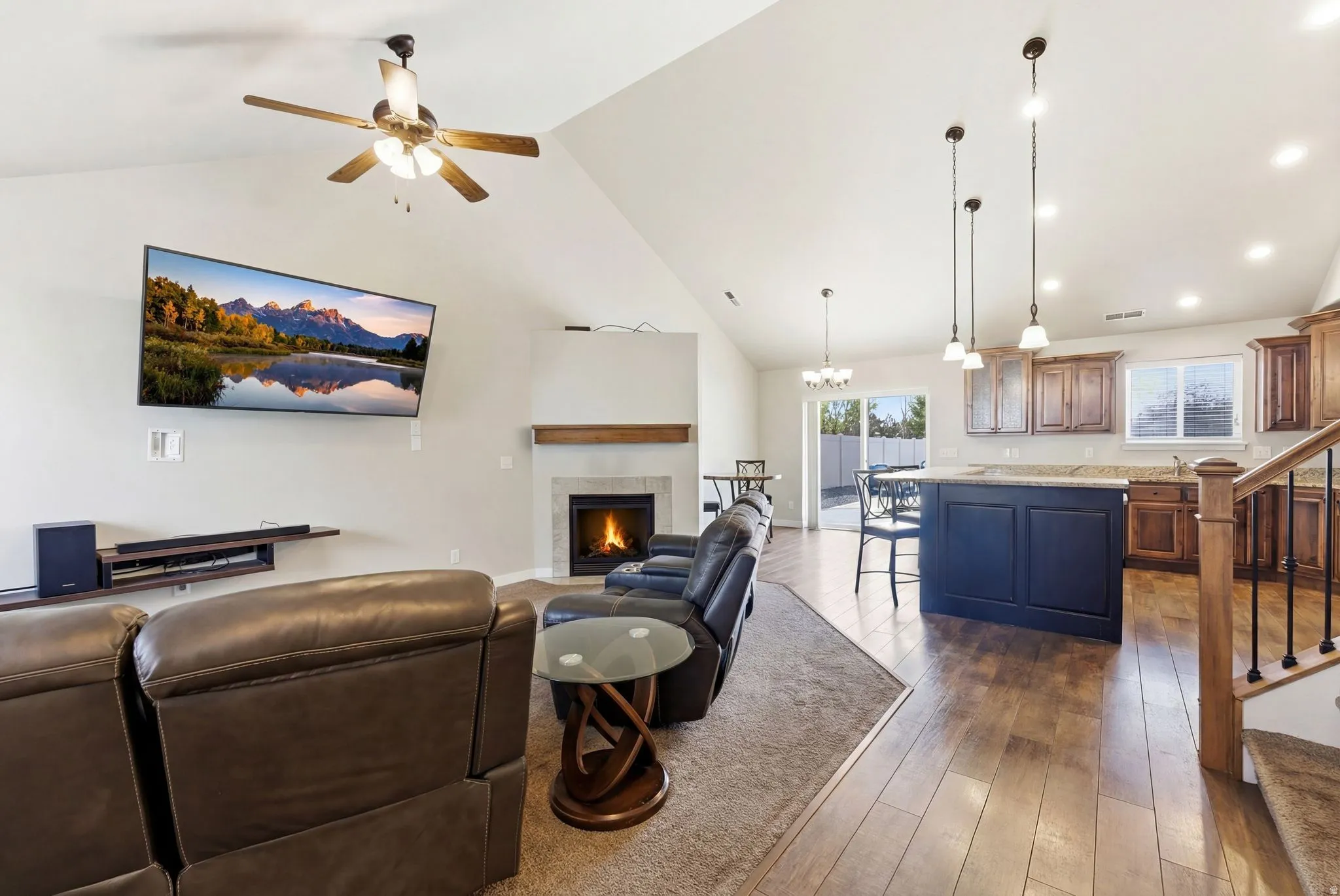 Living area featuring dark wood finished floors, a fireplace, a high ceiling, a ceiling fan, and suspended lighting