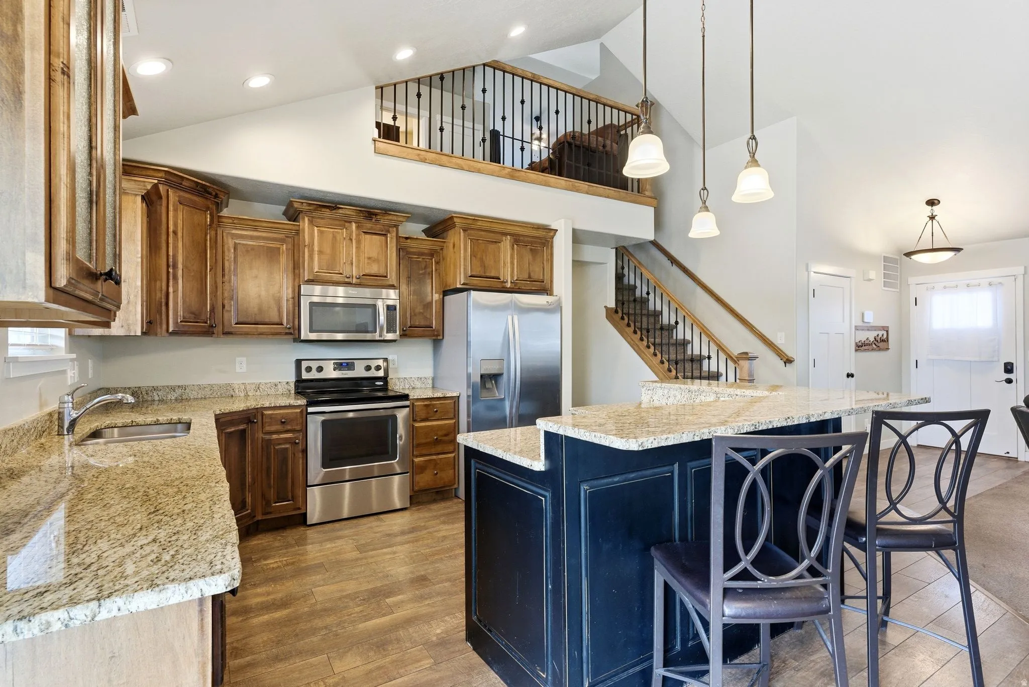 Kitchen with stainless steel appliances, a kitchen island, light stone counters, vaulted ceiling, and decorative light fixtures