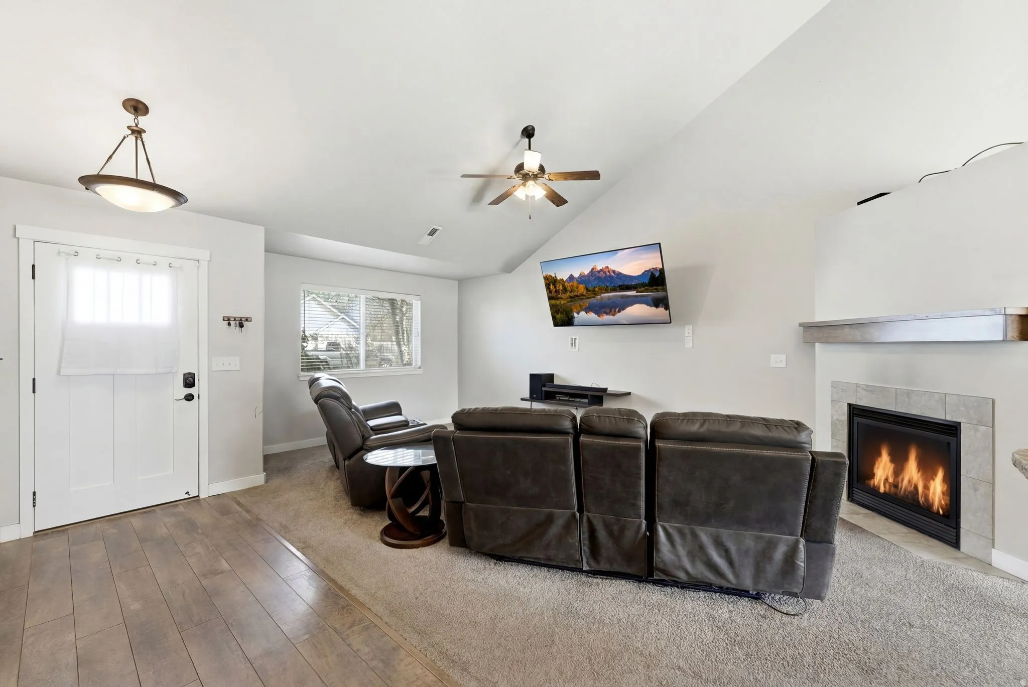 Carpeted living room with a fireplace, lofted ceiling, wood finished floors, and a ceiling fan