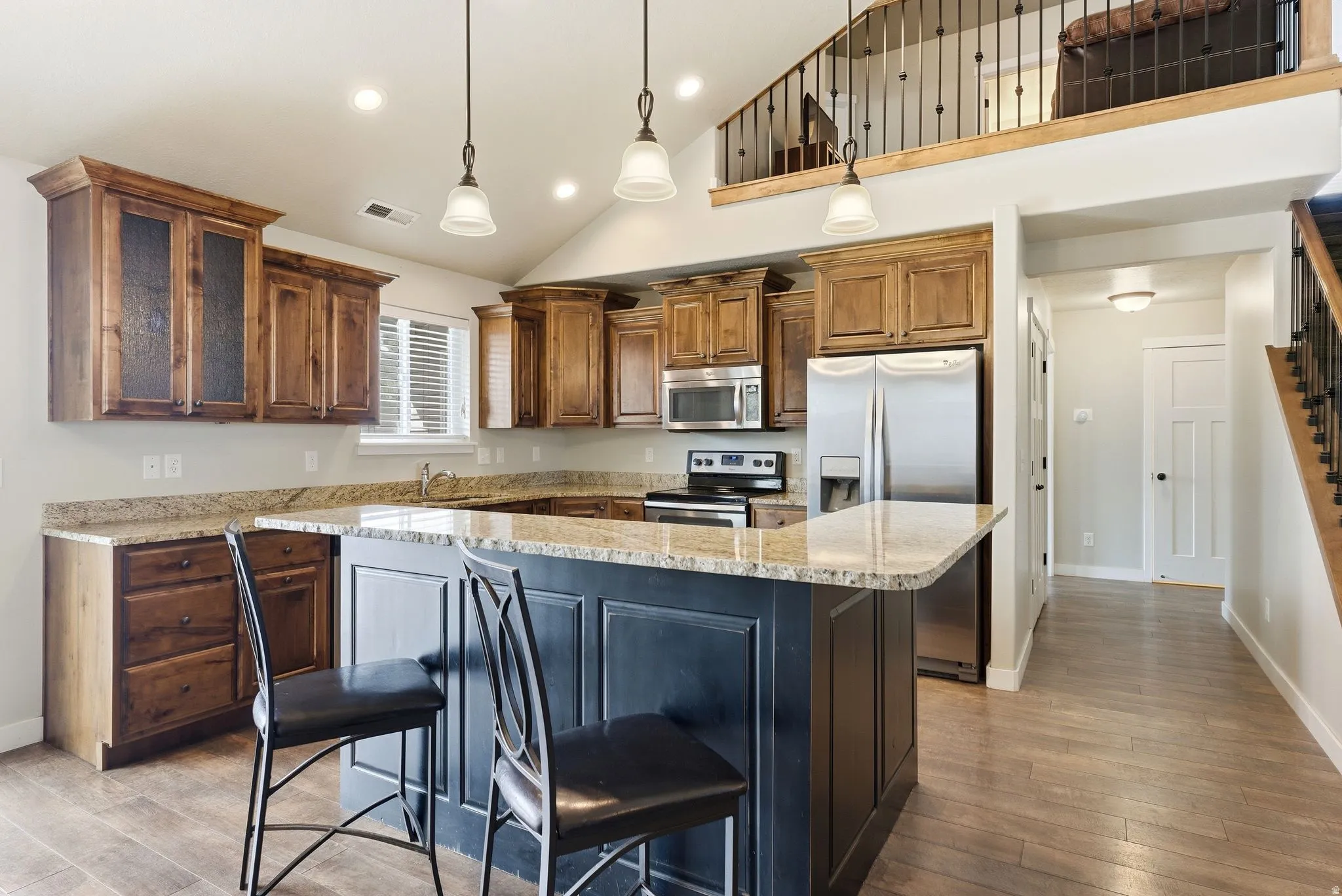 Kitchen with stainless steel appliances, light stone countertops, pendant lighting, a breakfast bar area, and vaulted ceiling