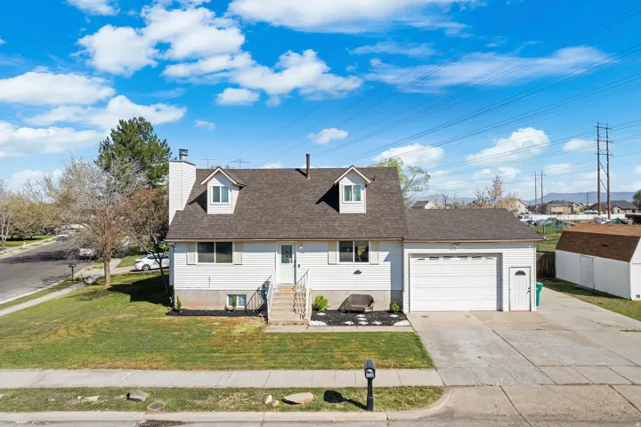 Cape cod-style house with a garage, driveway, a front yard, and a chimney