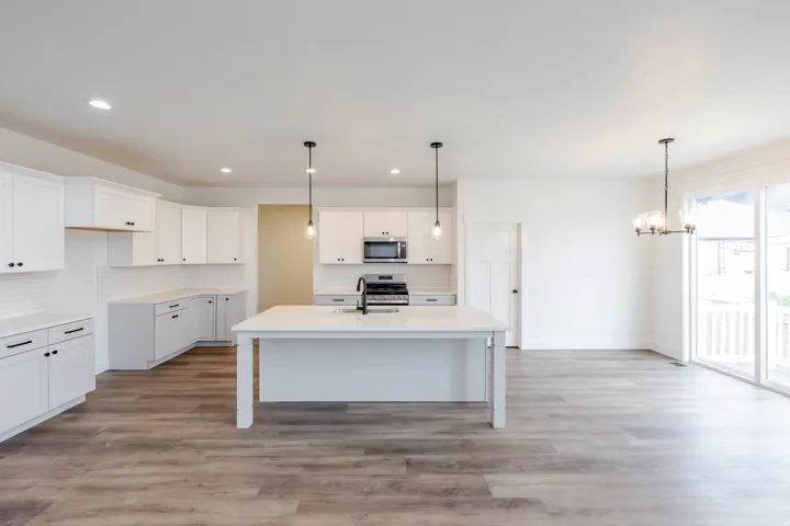 Open-concept kitchen featuring an expansive island with an integrated sink, white shaker cabinetry, stainless steel appliances, and wood-finish flooring