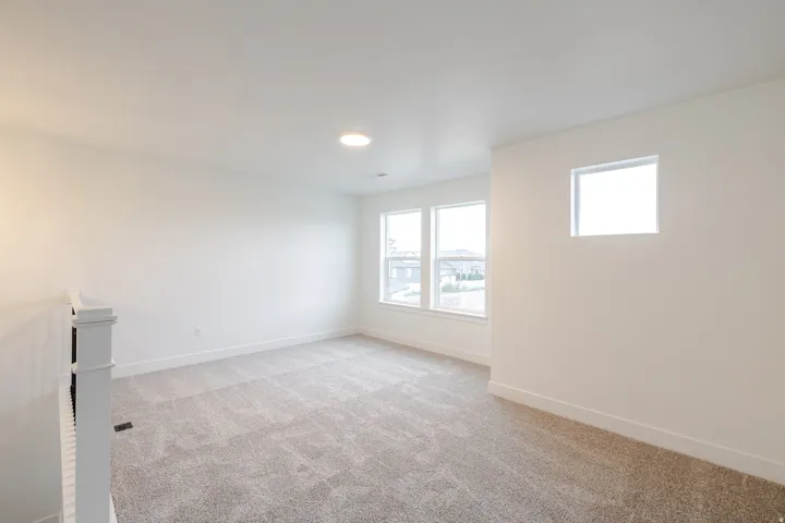Spacious room featuring neutral carpeting, multiple windows for abundant illumination, a contemporary flush-mount ceiling light, and a white balustrade