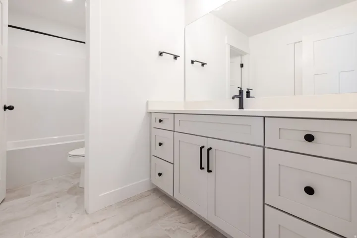 Contemporary bathroom featuring a light gray vanity with black hardware, a white countertop, and a large wall-mounted mirror