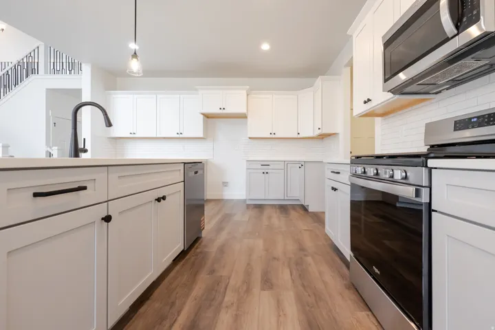 Modern kitchen featuring white shaker cabinetry, stainless steel appliances, a subway tile backsplash, and wood-finish flooring