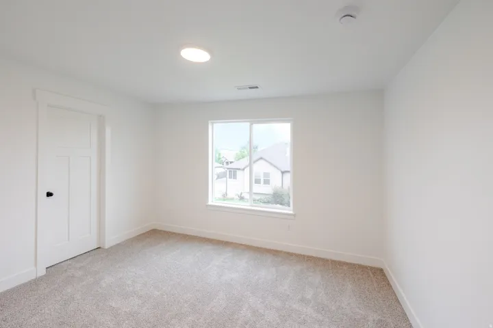 Carpeted room featuring a single window with white trim, a three-panel door with a black knob, a ceiling-mounted light fixture, and white baseboards