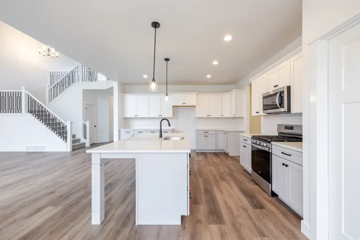 Open-concept kitchen featuring white cabinetry, stainless steel appliances, a white subway tile backsplash, and a central island with a sink and pendant lighting