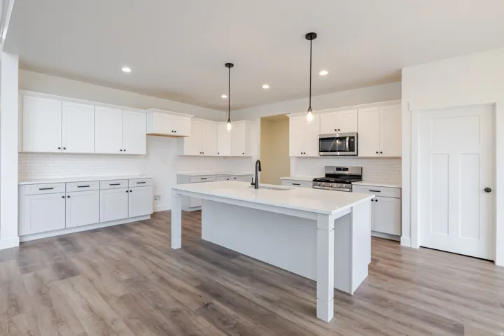 Open-concept kitchen featuring an expansive center island with a sink, white cabinetry with black hardware, subway tile backsplash, stainless steel appliances, and wood-finish flooring
