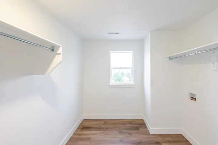 Bright utility room featuring wood-finish flooring, a single window, built-in shelving with a hanging rod, and laundry hookups