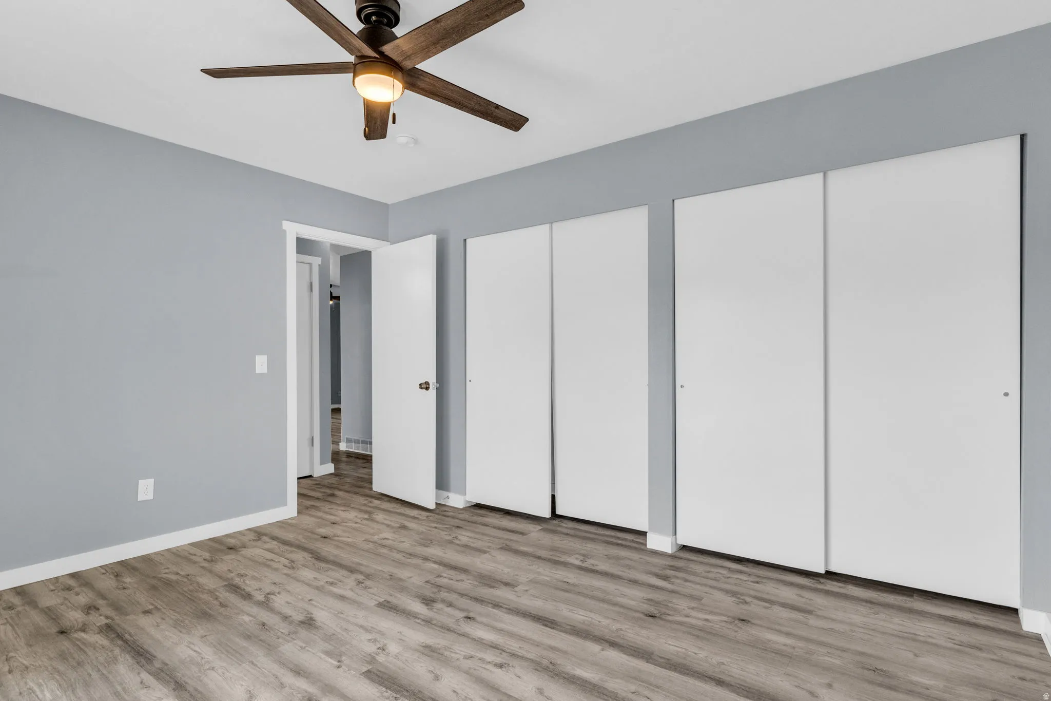 Unfurnished primary bedroom featuring multiple closets, light wood finished floors, and a ceiling fan