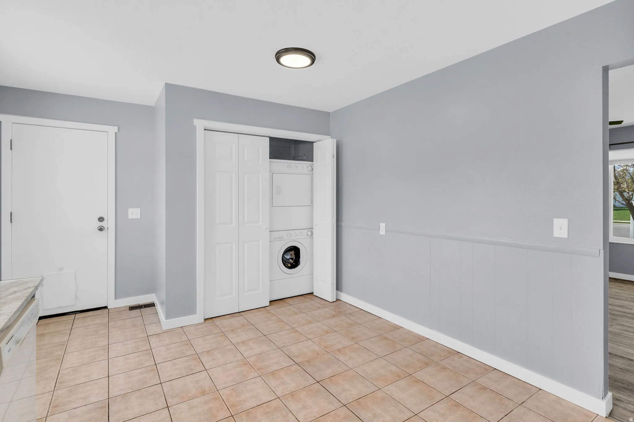 Laundry area with stacked washer / dryer, a wainscoted wall, and light tile patterned flooring