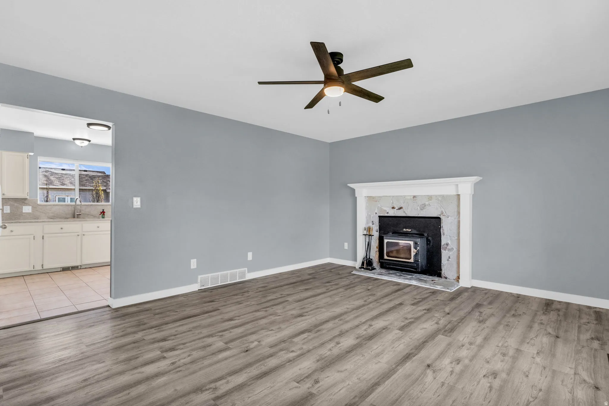 Unfurnished living room featuring light wood-type flooring, a ceiling fan, and a high end fireplace