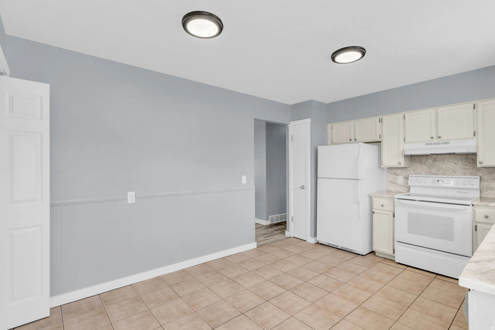 Kitchen with white appliances, wainscoting, decorative backsplash, and light tile patterned flooring