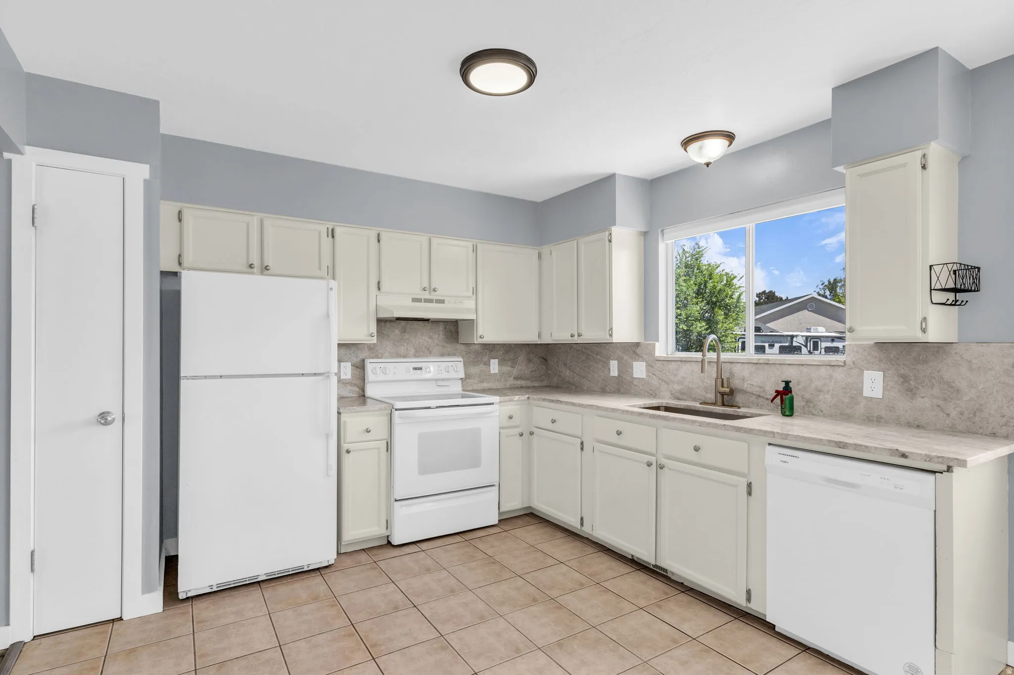 Kitchen with white appliances, white cabinets, light stone countertops, and light tile patterned floors