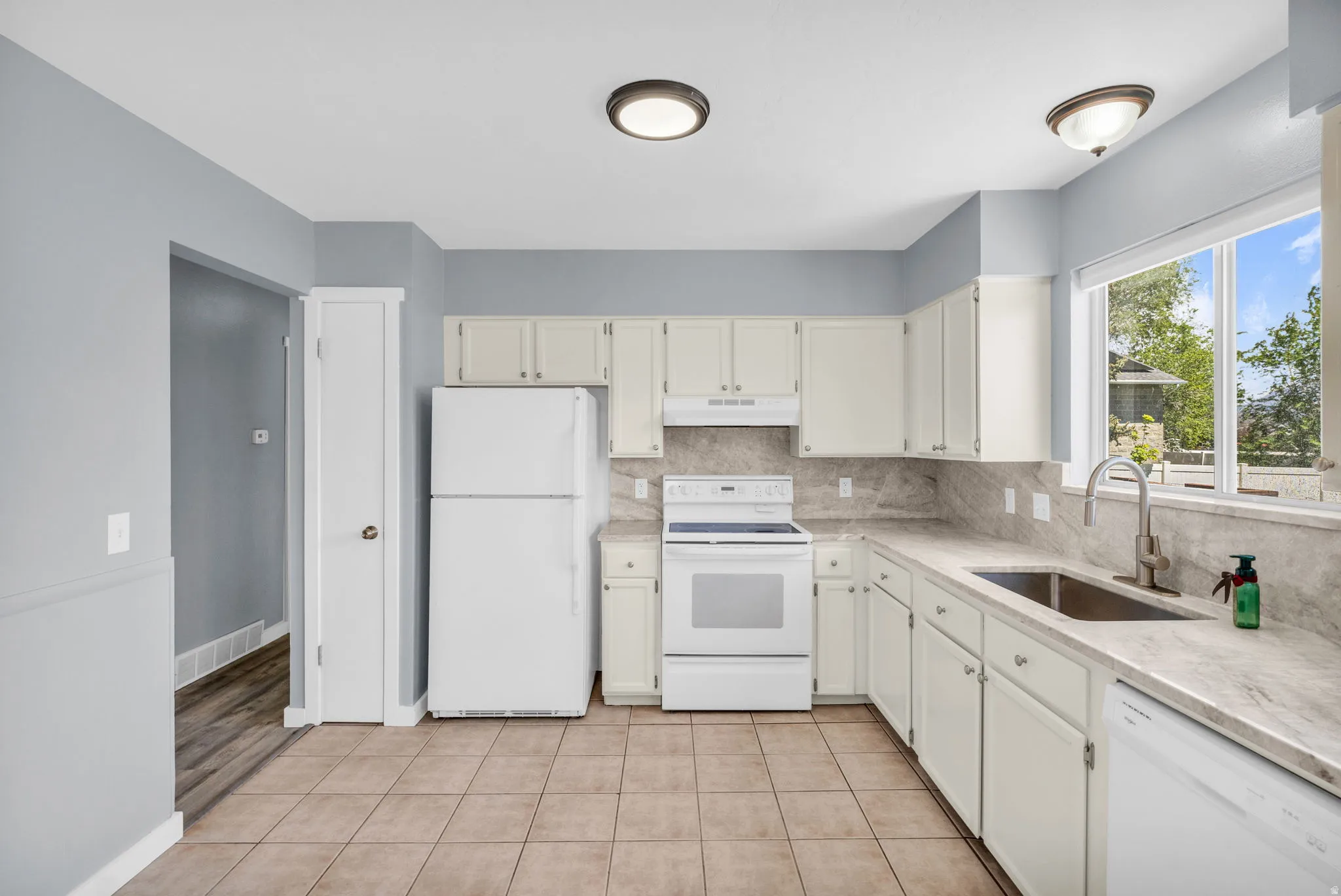Kitchen featuring white appliances, light tile patterned flooring, tasteful backsplash, and light stone countertops