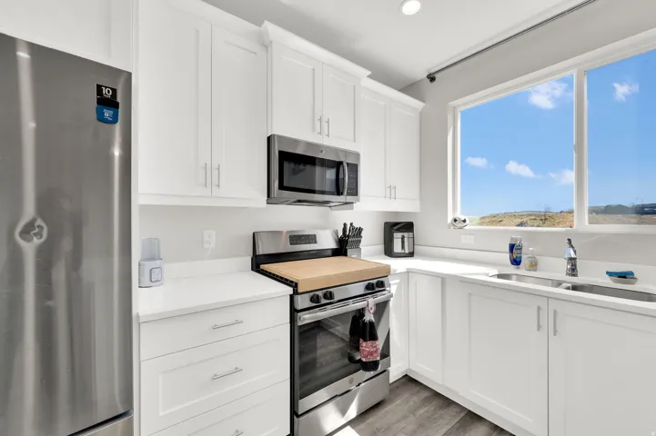 Kitchen featuring stainless steel appliances, white cabinetry, light wood-type flooring, light stone countertops, and recessed lighting