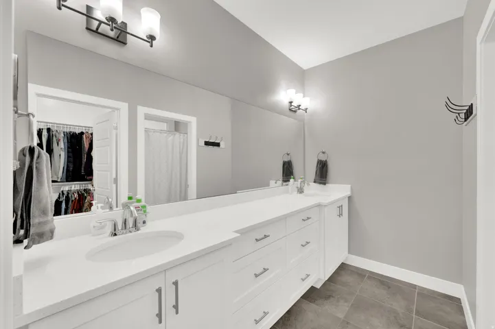 Bathroom with double vanity, a shower with curtain, dark tile patterned floors, and a spacious closet