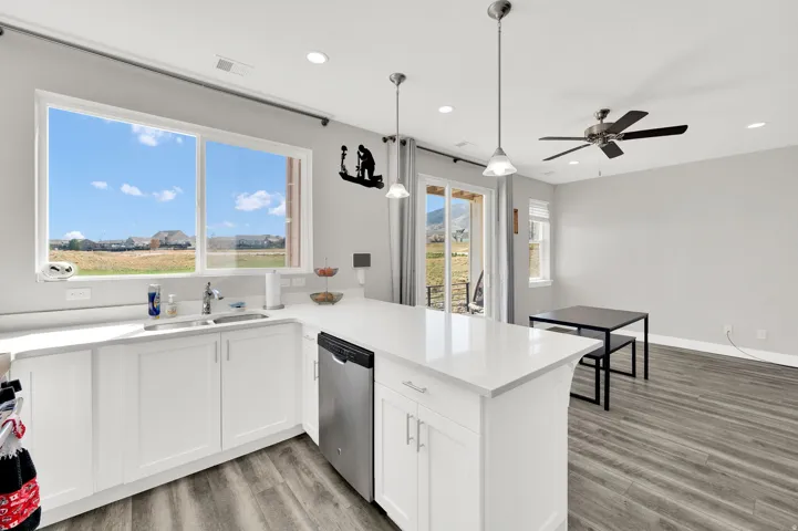 Kitchen featuring light wood-style floors, a peninsula, stainless steel dishwasher, pendant lighting, and white cabinetry