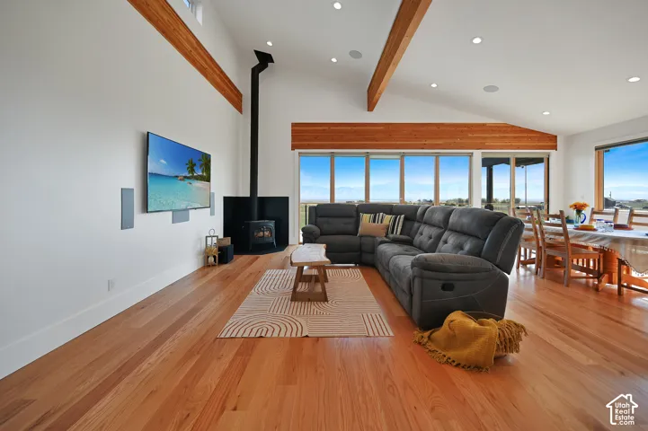 Vaulted ceilings with exposed wood beams, wood-finish flooring, recessed lighting, and a corner wood-burning stove with a black surround