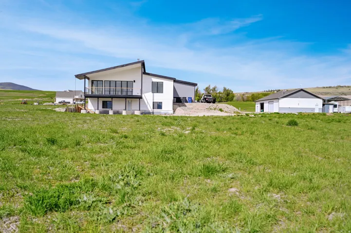 Back of house featuring a balcony, a mountain view, stucco siding, and a view of rural / pastoral area