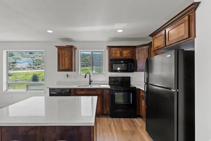 Kitchen featuring black appliances, dark wood finish cabinets, light wood-style flooring, recessed lighting, and a center island