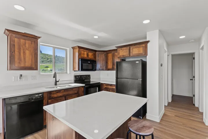 Kitchen with black appliances, light wood-style floors, a kitchen island, light stone countertops, and recessed lighting