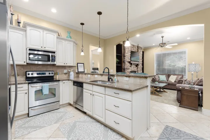 Kitchen featuring a ceiling fan, stainless steel appliances, a peninsula, white cabinets, and light stone counters