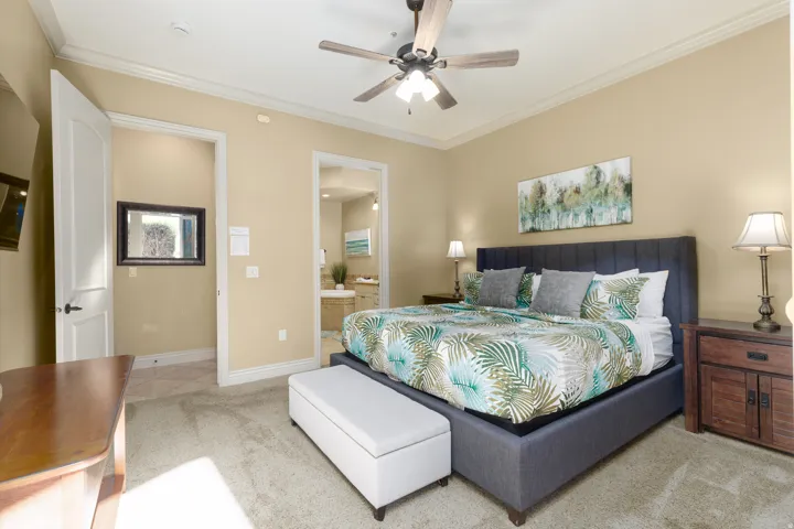 Primary bedroom with en suite bathroom, ornamental molding, a ceiling fan, and light carpet