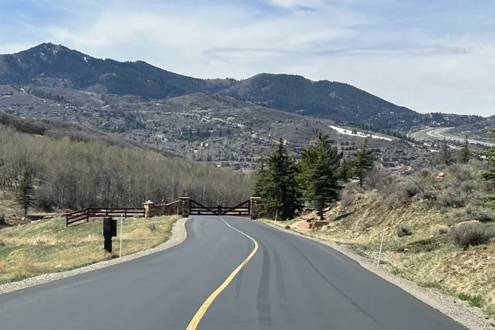 Paved road with central yellow line, stone pillar gate with wooden fence, and mountainous backdrop