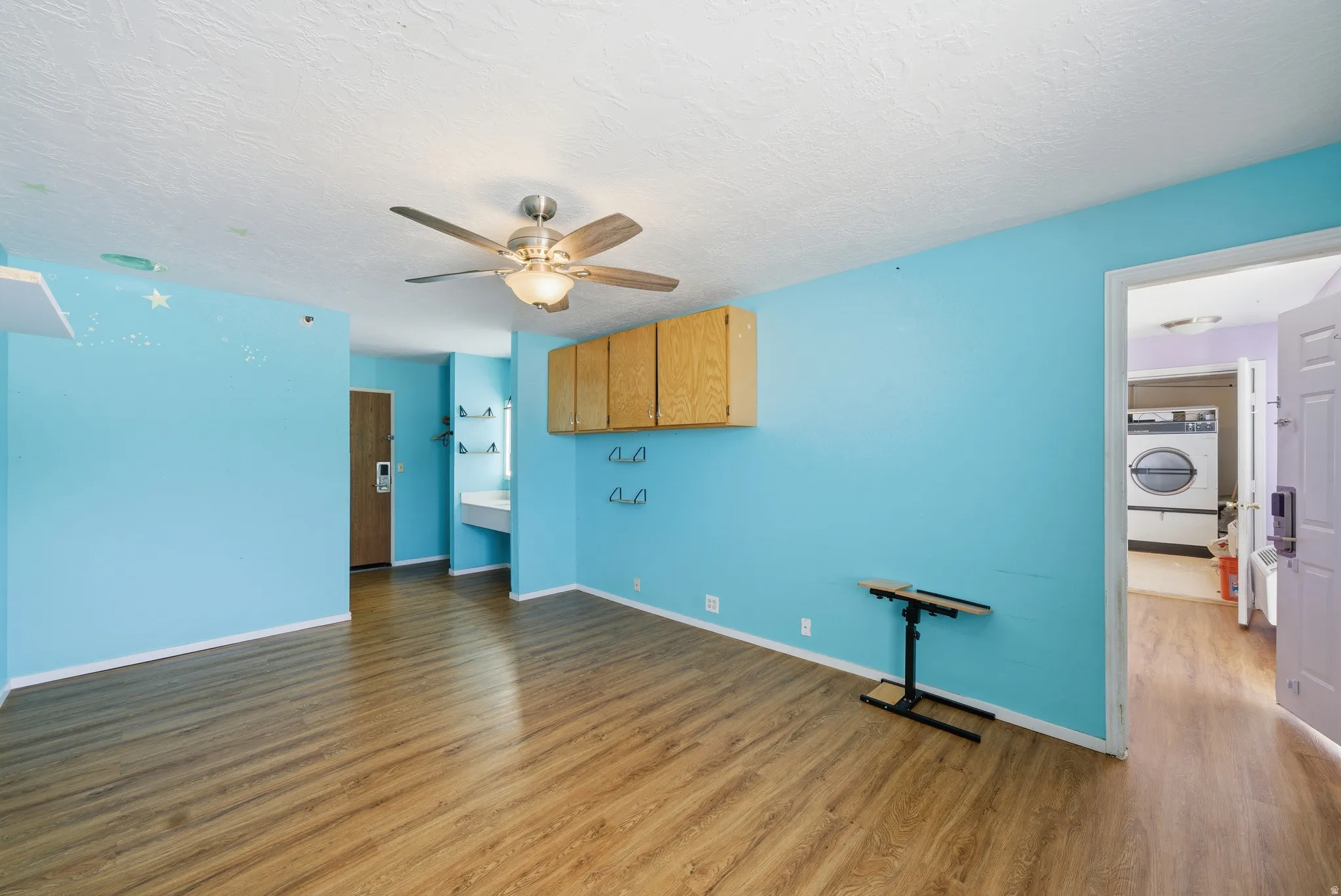 Empty room with wood finished floors, washer / dryer, ceiling fan, and a textured ceiling