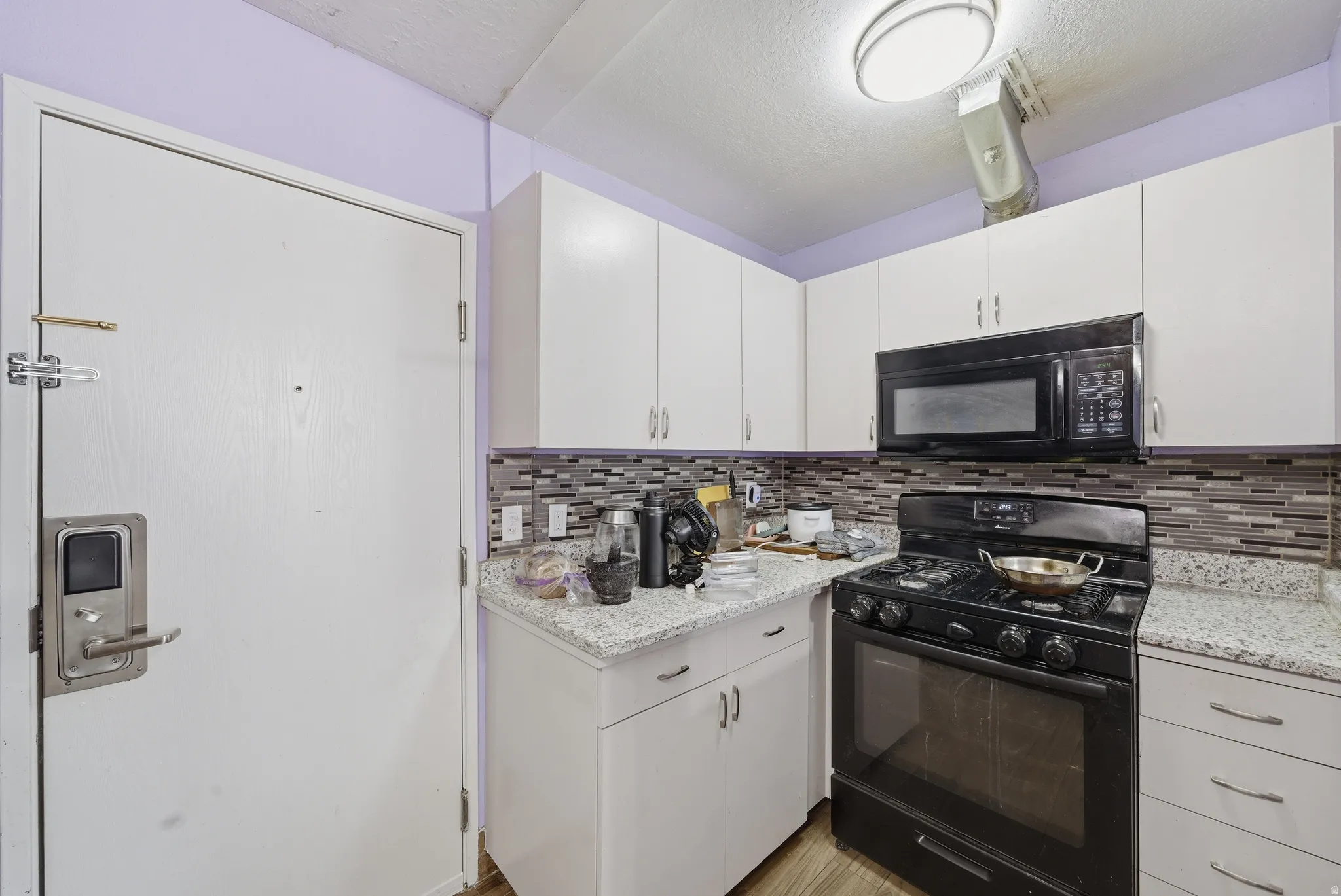 Kitchen with black appliances, white cabinetry, a textured ceiling, and light stone countertops